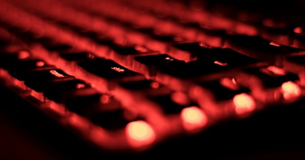 Primer plano de un teclado de ordenador bajo una luz roja, que simboliza la protección de la ciberocupación